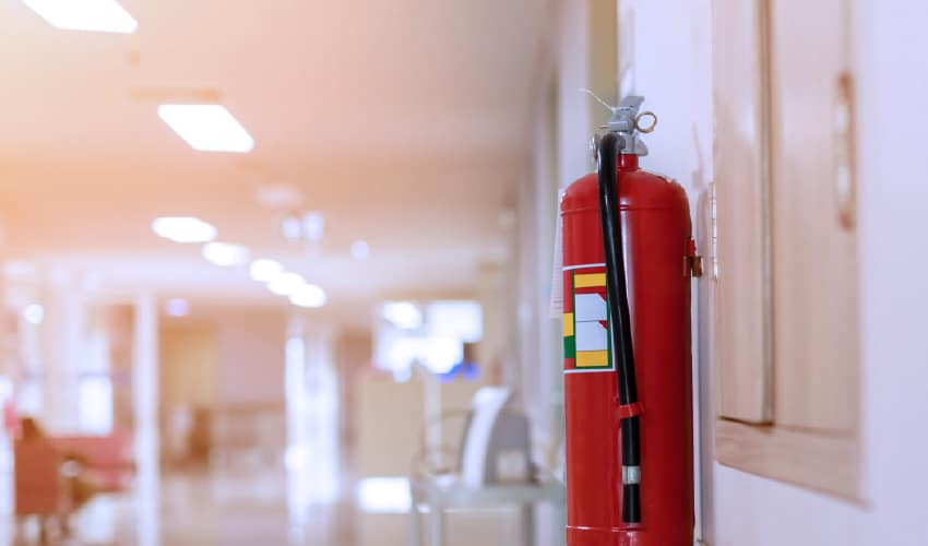 A fire extinguisher mounted on a wall in the hallway of a hospital or healthcare facility
